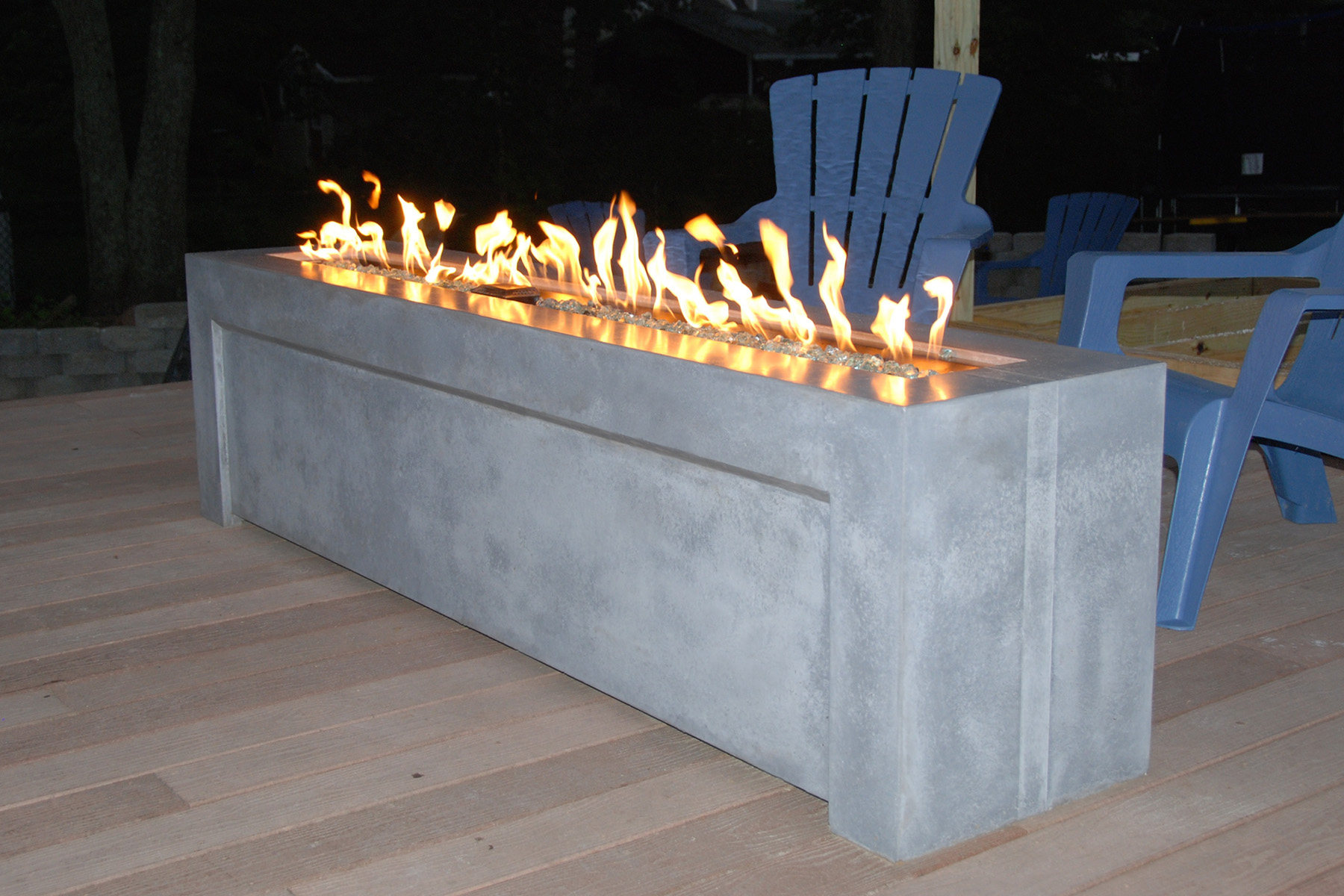 long rectangular gray concrete fire pit lit with blue Adirondack chairs