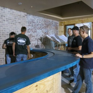 five men installing large curved blue concrete bartop
