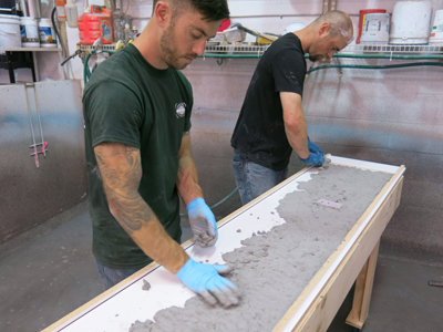 two men placing light gray concrete in molds