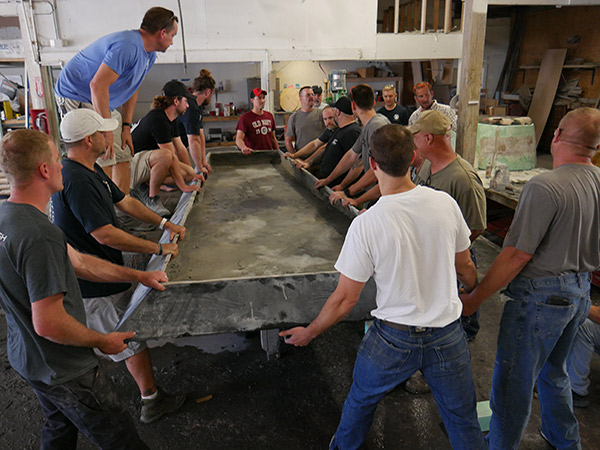 lots of men gathered around large concrete table top on casting table